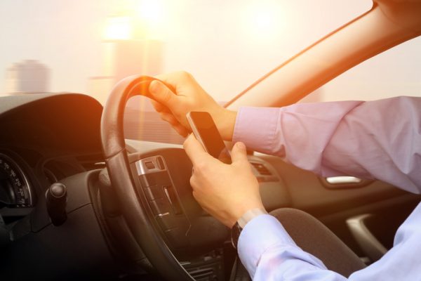 person driving car while looking at smart phone screen