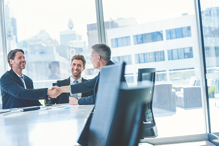 smiling business men shake hands at a large conference table